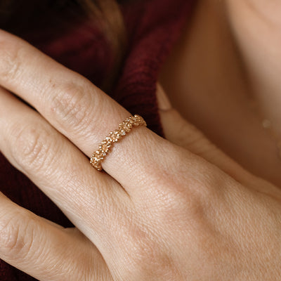 Close up of a hand with a gold floral-etched ring band with textured cherry blossom flowers and small clear gemstones.