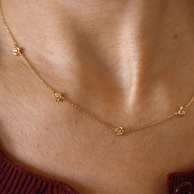 A lifestyle image of a dainty gold necklace on a person's neck with stationary textured cherry blossom flowers with small accent stones in the center along the chain.
