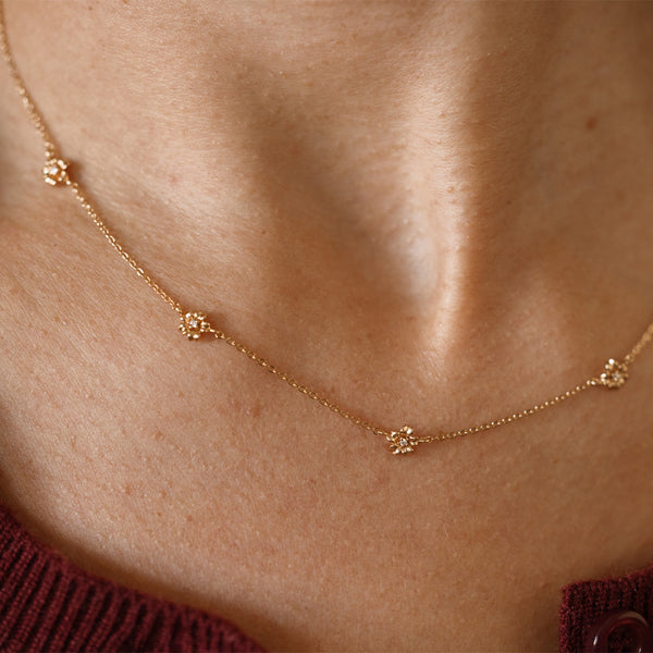 A lifestyle image of a dainty gold necklace on a person's neck with stationary textured cherry blossom flowers with small accent stones in the center along the chain.
