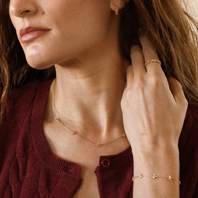 A close-up of a model wearing a dainty gold necklace with cherry blossom flower stations, plus a matching bracelet and ring.