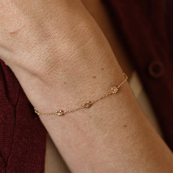 A lifestyle image of a dainty gold bracelet on a person's wrist with stationary textured cherry blossom flowers with small accent stones in the center along the chain.