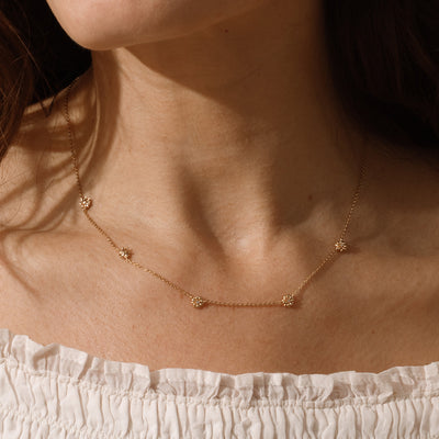 A lifestyle image of a dainty gold necklace on a person's neck with stationary textured daisy flowers with small accent stones in the center along the chain.