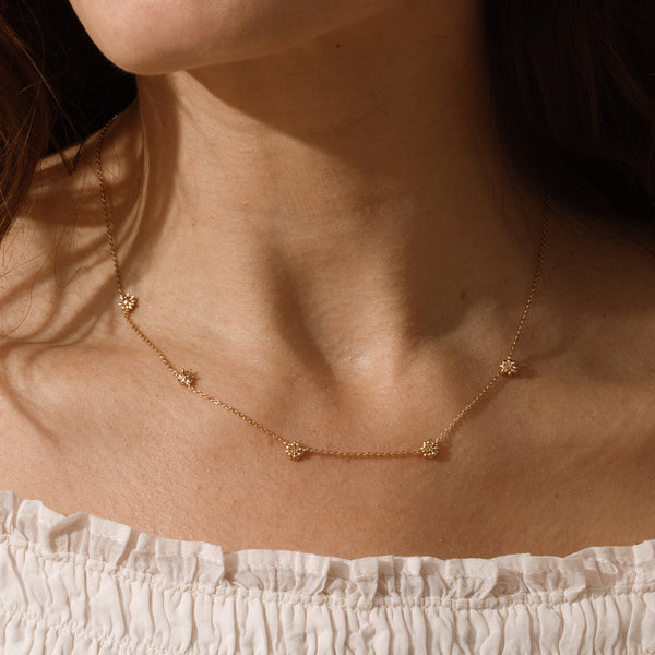 A lifestyle image of a dainty gold necklace on a person's neck with stationary textured daisy flowers with small accent stones in the center along the chain.