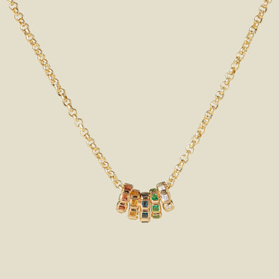 A gold vermeil necklace with a series of multicolored birthstone spacer charms, set against a solid beige background.