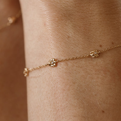 A lifestyle image of a dainty gold bracelet on a person's wrist with stationary textured lily of the valley flowers with small accent stones in the center along the chain.