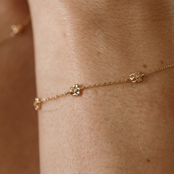 A lifestyle image of a dainty gold bracelet on a person's wrist with stationary textured lily of the valley flowers with small accent stones in the center along the chain.