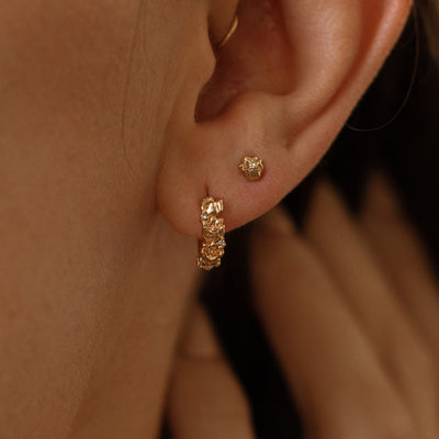 Close-up of a person wearing gold hoop earrings made up of a textured floral design and a matching stud earring with a singular floral motif.