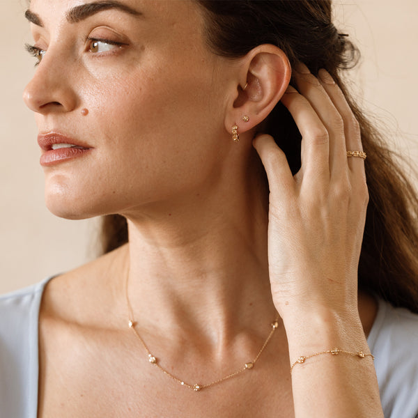 Woman wearing gold jewelry adorned with different textured flowers, including earrings, necklace, and bracelet against a neutral background