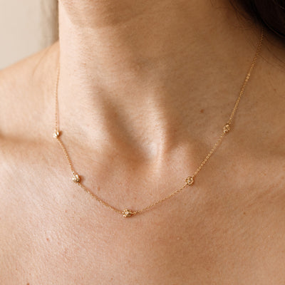 A lifestyle image of a dainty gold necklace on a person's neck with stationary textured lily of the valley flowers with small accent stones in the center along the chain.