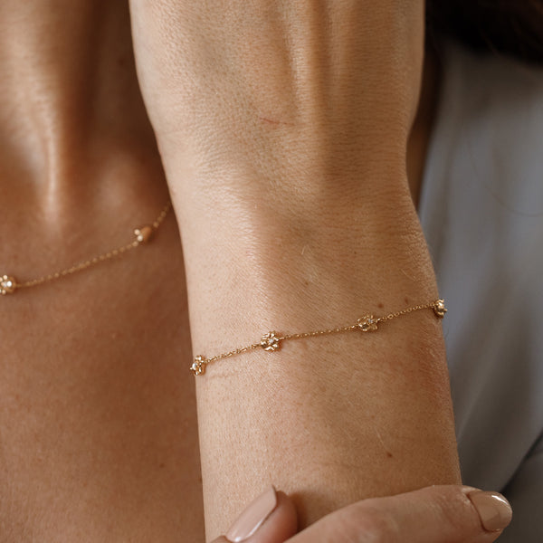 A lifestyle image of a dainty gold bracelet on a person's wrist with stationary textured lily of the valley flowers with small accent stones in the center along the chain.