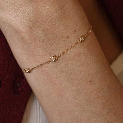 A lifestyle image of a dainty gold bracelet on a person's wrist with stationary textured rose flowers with small accent stones in the center along the chain.
