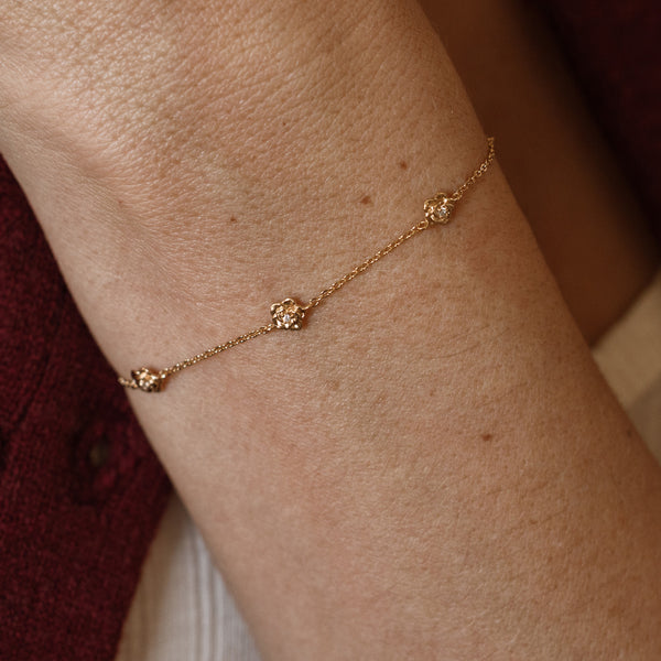 A lifestyle image of a dainty gold bracelet on a person's wrist with stationary textured rose flowers with small accent stones in the center along the chain.