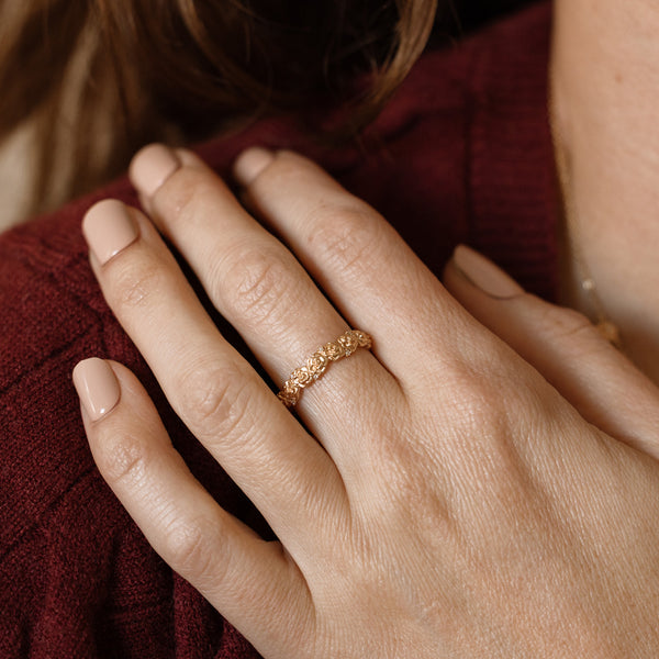 Close up of a hand with a gold floral-etched ring band with textured rose flowers and small clear gemstones.