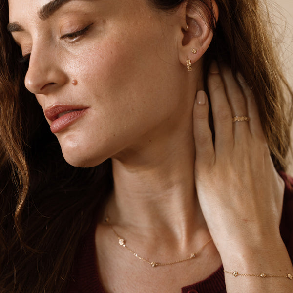 Close-up of a woman wearing gold jewelry with flowers on them, including earrings, necklace, and bracelet.