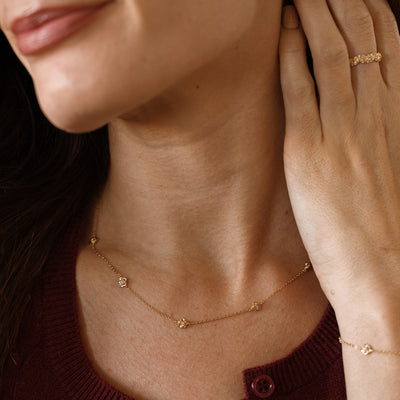 A lifestyle image of a dainty gold necklace on a person's neck with stationary textured rose flowers with small accent stones in the center along the chain.
