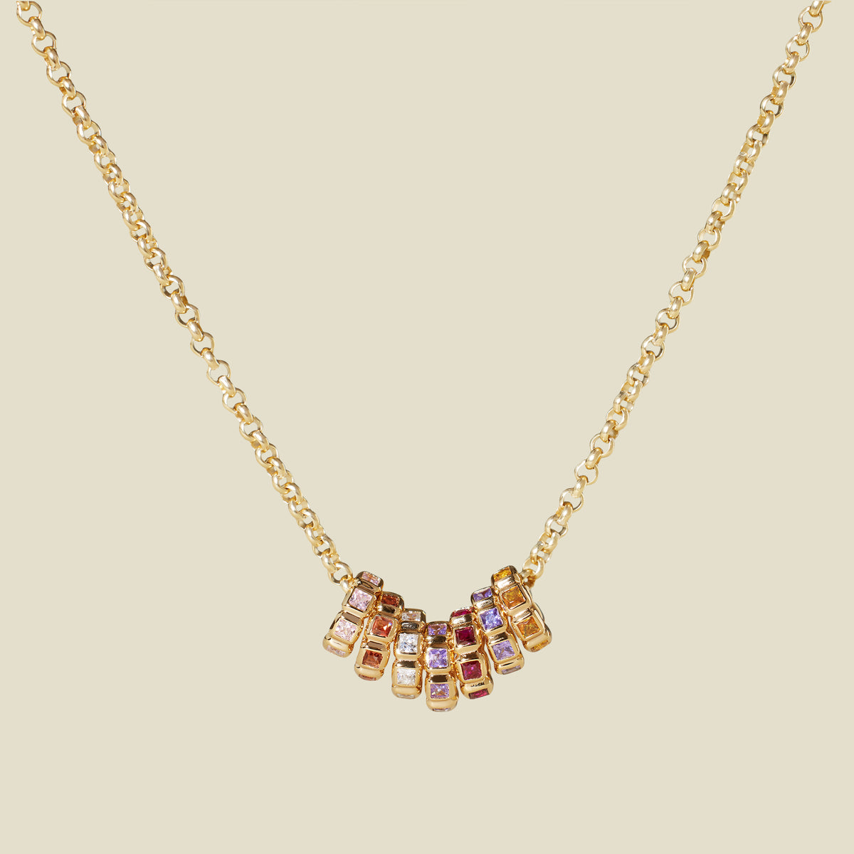 A gold vermeil necklace with a series of multicolored birthstone spacer charms, set against a solid beige background.
