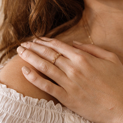 Close up of a hand with a gold floral-etched ring band with textured lotus flowers and small clear gemstones.