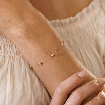 A lifestyle image of a dainty gold bracelet on a person's wrist with stationary textured lotus flowers with small accent stones in the center along the chain.