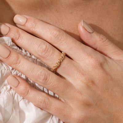 Close up of a hand with a gold floral-etched ring band with textured lotus flowers and small clear gemstones.