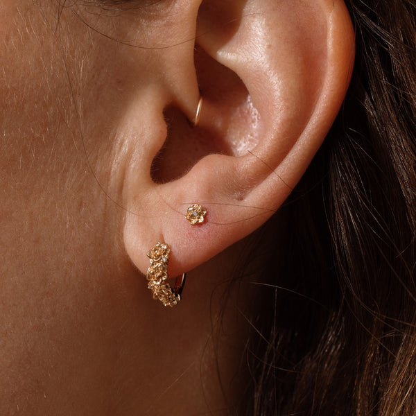 Close-up of a person wearing gold hoop earrings made up of a textured floral design and a matching stud earring