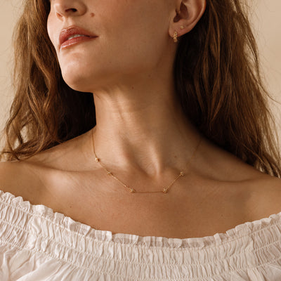 A lifestyle image of a dainty gold necklace on a person's neck with stationary textured lotus flowers with small accent stones in the center along the chain.