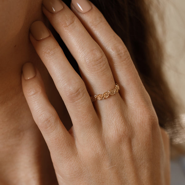 Close up of a hand with a gold floral-etched ring band with textured poppy flowers and small clear gemstones.