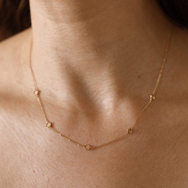 A lifestyle image of a dainty gold necklace on a person's neck with stationary textured poppy flowers with small accent stones in the center along the chain.