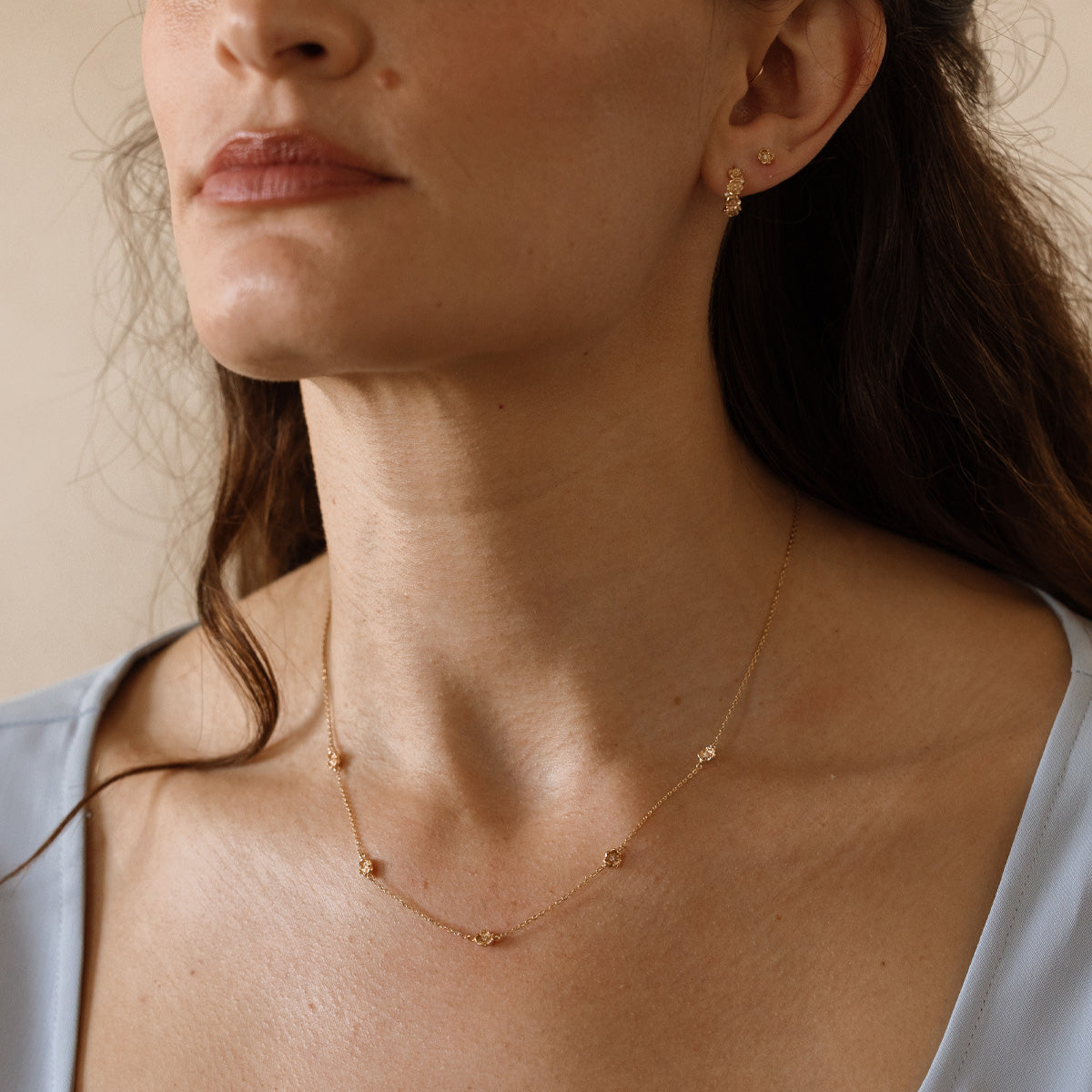 A lifestyle image of a dainty gold necklace on a person's neck with stationary textured poppy flowers with small accent stones in the center along the chain.