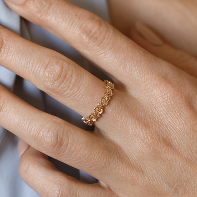 Close up of a hand with a gold floral-etched ring band with textured poppy flowers and small clear gemstones.