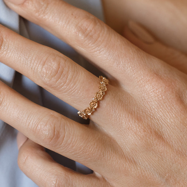 Close up of a hand with a gold floral-etched ring band with textured poppy flowers and small clear gemstones.