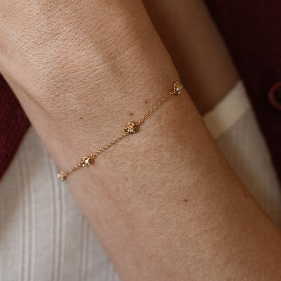 A lifestyle image of a dainty gold bracelet on a person's wrist with stationary textured peony flowers with small accent stones in the center along the chain.