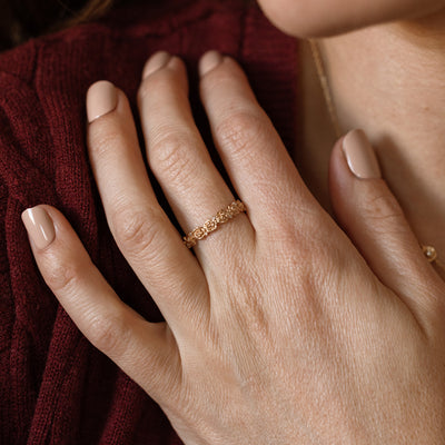 Close up of a hand with a gold floral-etched ring band with textured peony flowers and small clear gemstones.