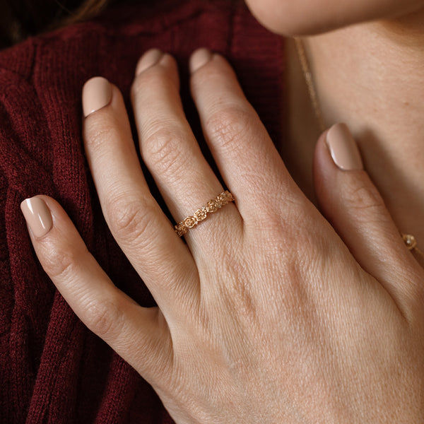 Close up of a hand with a gold floral-etched ring band with textured peony flowers and small clear gemstones.