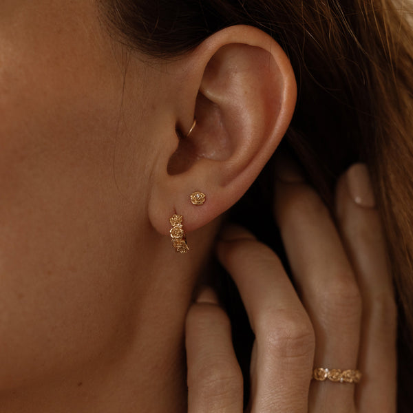 Close-up of a person wearing gold hoop earrings made up of a floral design and a matching stud earring, with a hand adjusting them.