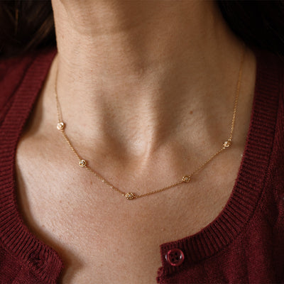 A lifestyle image of a dainty gold necklace on a person's neck with stationary textured peony flowers with small accent stones in the center along the chain.