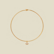 A delicate gold wire circle necklace with a small oval bezel-set clear gemstone pendant, displayed on a solid light beige background.