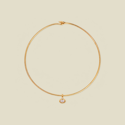 A delicate gold wire circle necklace with a small oval bezel-set clear gemstone pendant, displayed on a solid light beige background.