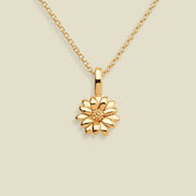 A gold daisy pendant necklace on a delicate gold chain, set against a solid light beige background.
