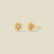 A pair of gold daisy flower stud earrings, each featuring a small round clear gemstone at the center, displayed on a solid light beige background.