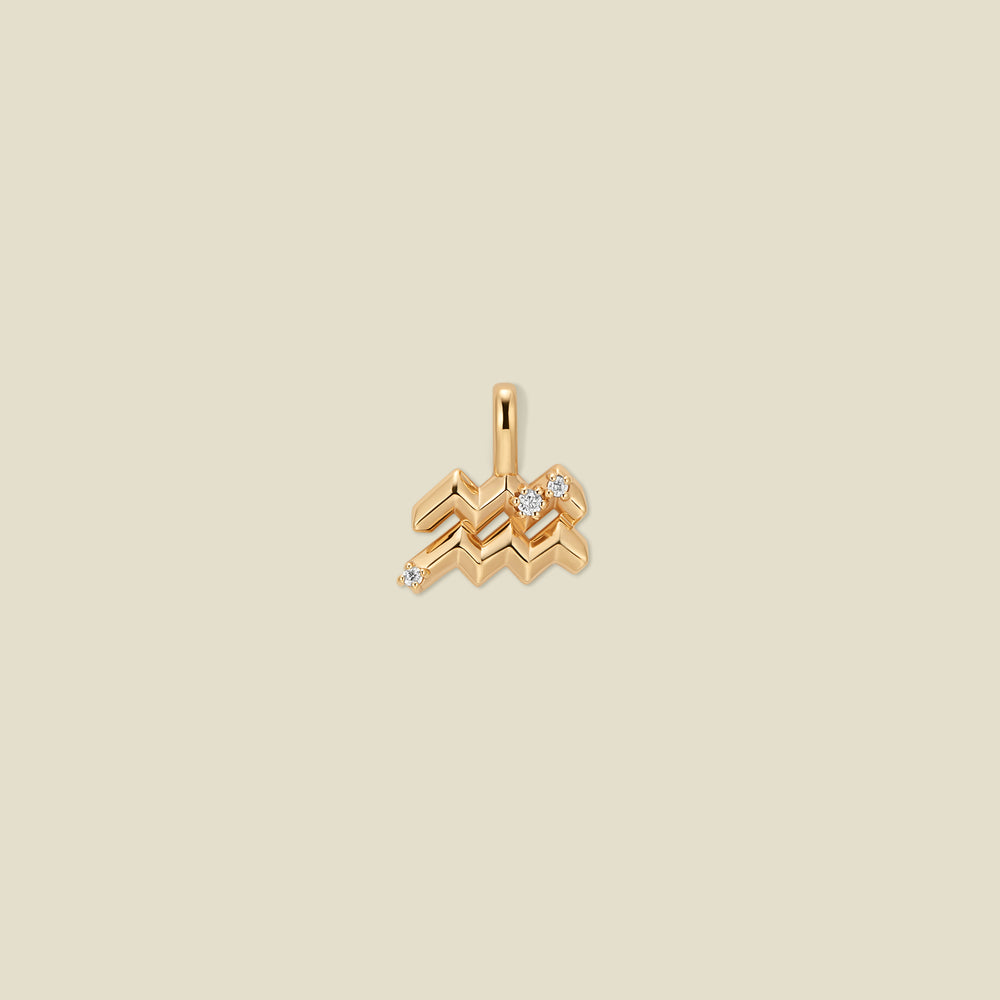 A gold pendant shaped like the Aquarius zodiac symbol, featuring three small clear gemstones, centered on a solid light beige background.