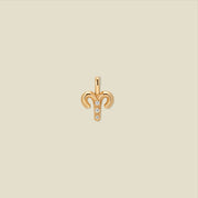 A gold pendant shaped like the Aries zodiac symbol, featuring three small clear gemstones, centered on a solid light beige background.