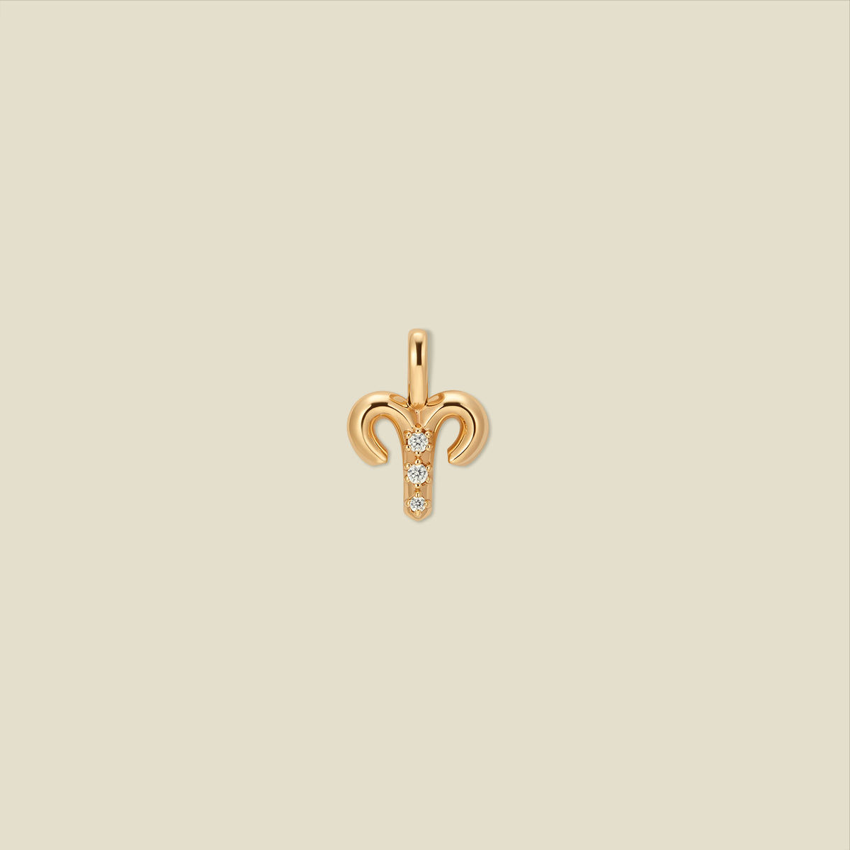 A gold pendant shaped like the Aries zodiac symbol, featuring three small clear gemstones, centered on a solid light beige background.