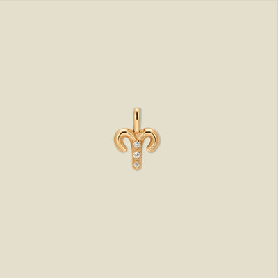 A gold pendant shaped like the Aries zodiac symbol, featuring three small clear gemstones, centered on a solid light beige background.