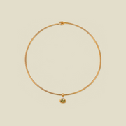 A delicate gold wire necklace with a small oval pendant featuring a green gemstone, displayed on a solid light beige background.