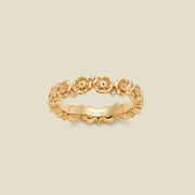 A gold floral-etched ring band with textured poppy flowers and small clear gemstones, shown on a plain warm beige background. 