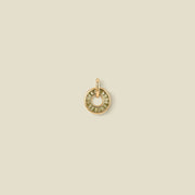 A circular gold pendant featuring light green baguette-cut stones around a hollow center, displayed against a solid light beige background.