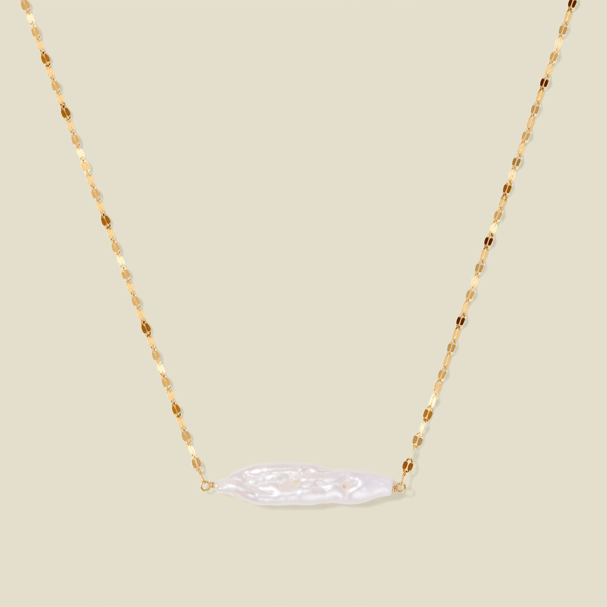 Gold lace chain with a baroque pearl pendant, suspended against a neutral background.