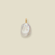 A single baroque pearl pendant with an iridescent white surface and a small gold bail, centered on a solid beige background.