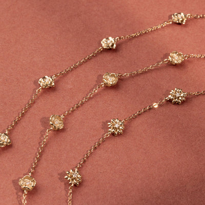 Three delicate gold chain bracelets, each featuring five ornate, textured gold flower charms with small clear stones, arranged side by side on a red background.