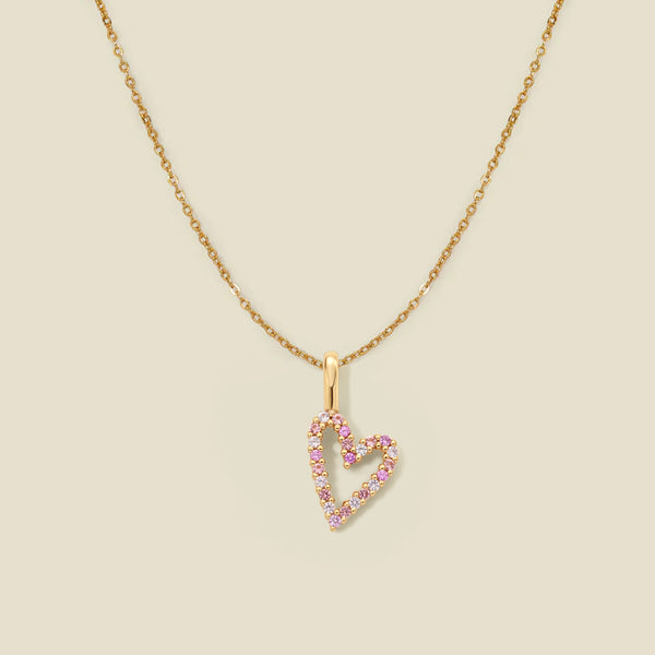 A delicate gold chain necklace featuring a heart-shaped pendant outlined with small pink gemstones, set against a solid light beige background.